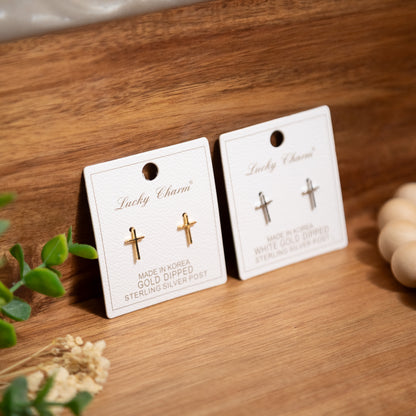 Two pairs of earrings on 'Lucky Charm' cards on a wooden surface with plants.