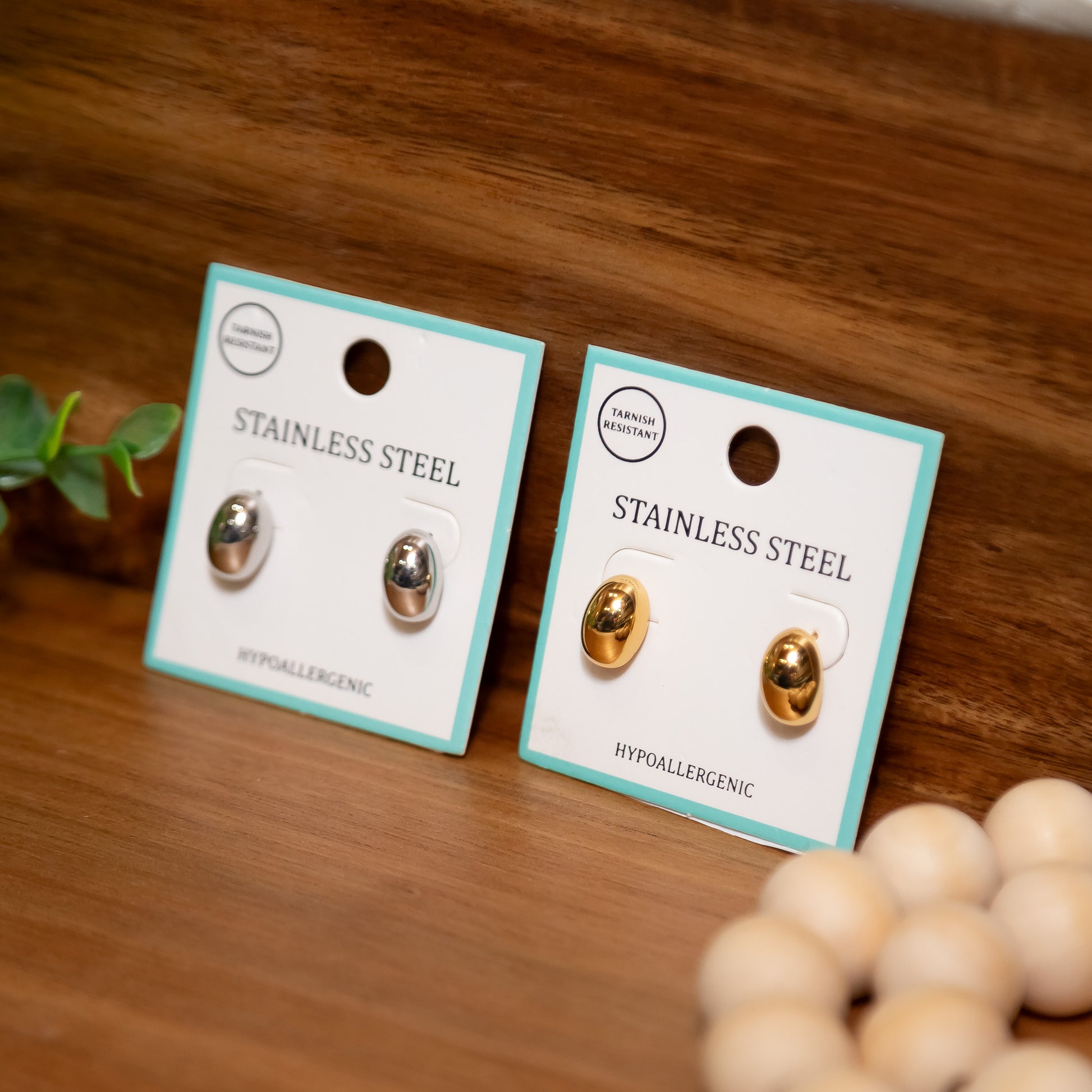 Two pairs of stainless steel earrings on cards with a wooden background