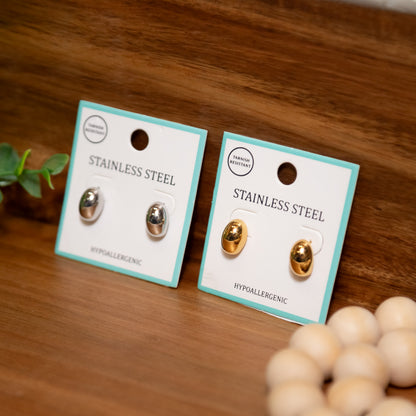 Two pairs of stainless steel earrings on cards with a wooden background