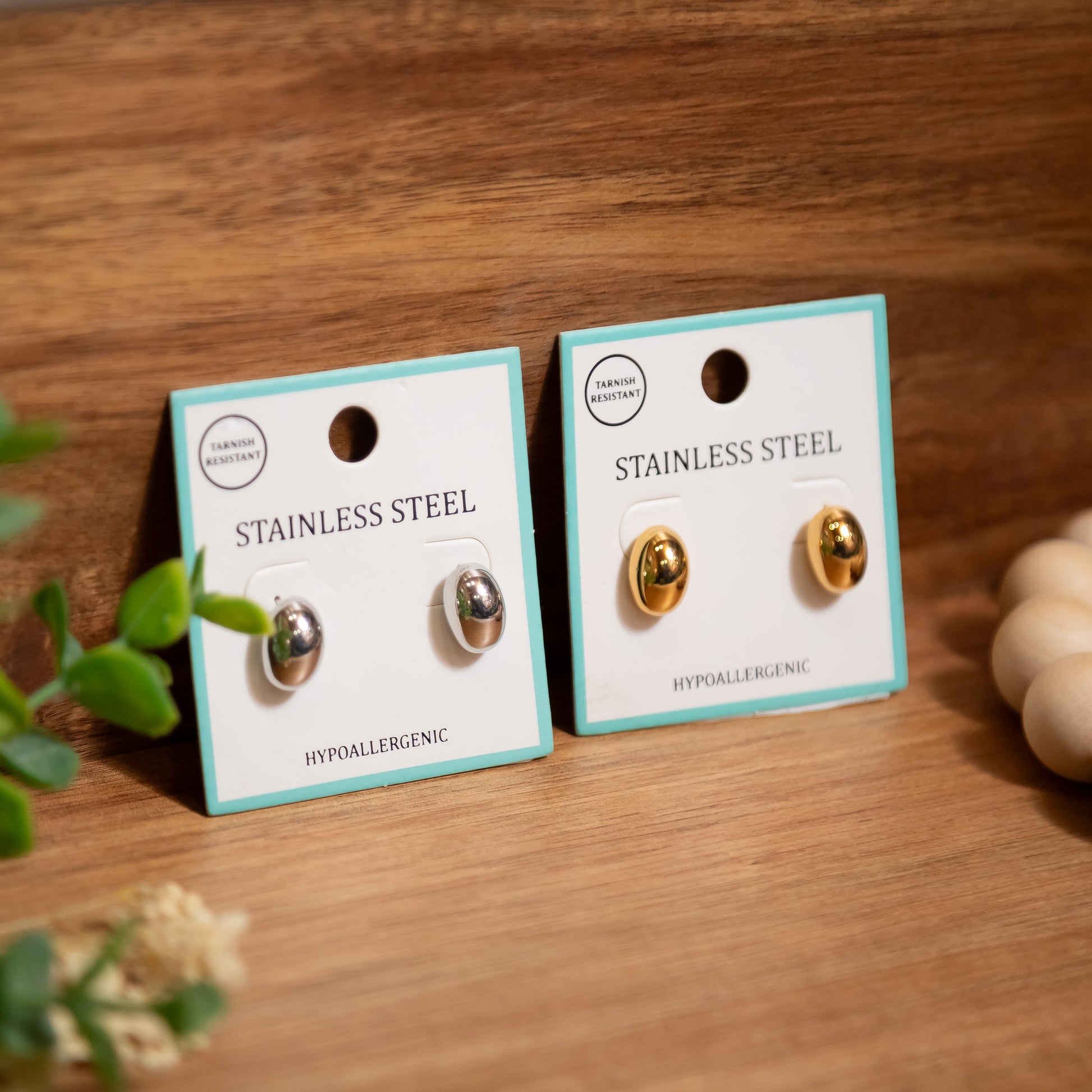 Two pairs of stainless steel earrings on display cards with a wooden background.