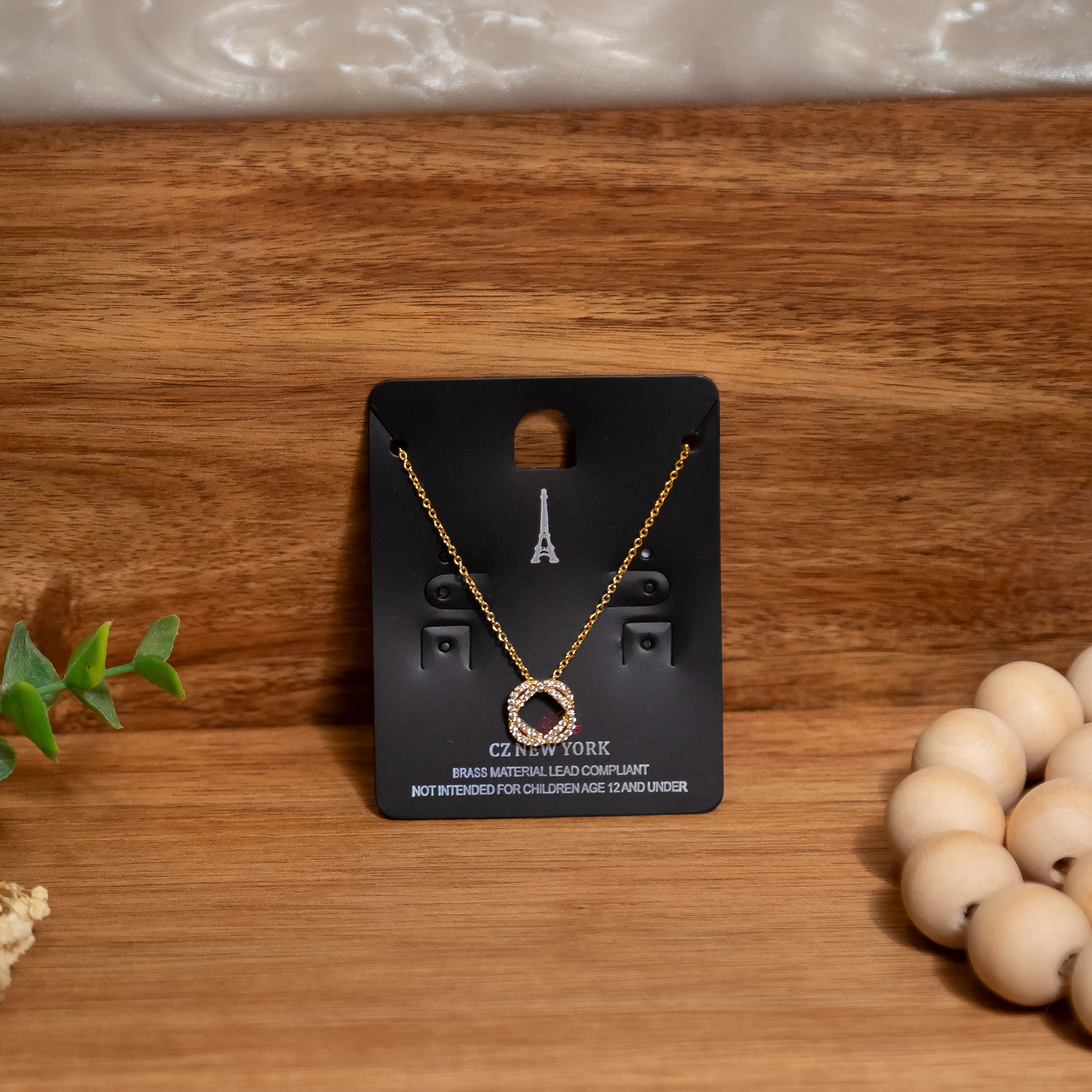 Gold necklace on a black card with 'CZ New York' branding on a wooden surface.