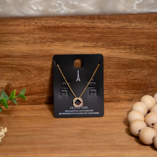 Gold necklace on a black card with 'CZ New York' branding on a wooden surface.