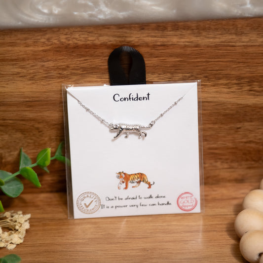 Silver necklace with a tiger design on a card with text, placed on a wooden surface.