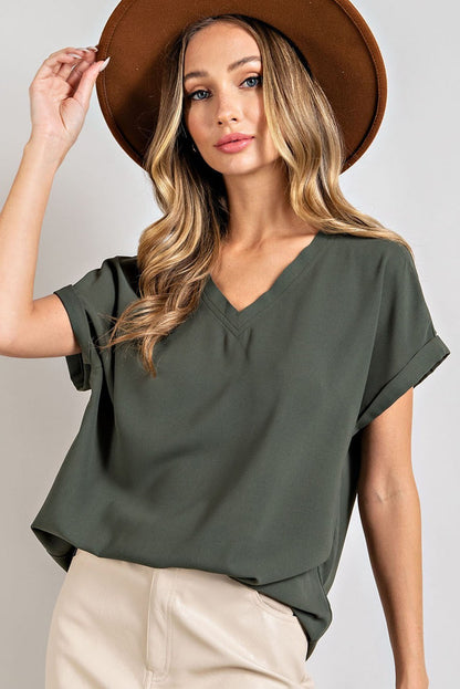 A woman wearing a green V-neck top with cuffed short sleeves, paired with beige pants and a wide-brim hat.