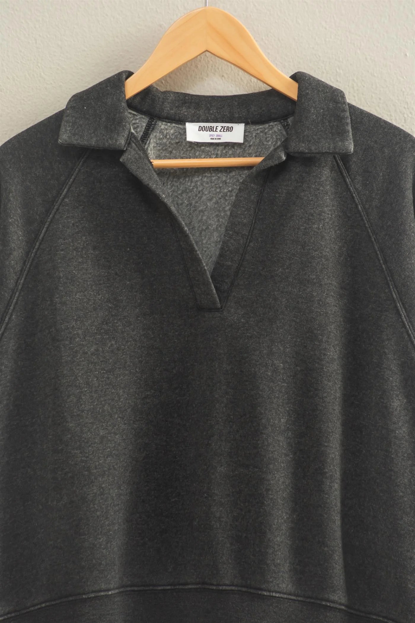 “Raglan sleeve sweatshirt with collar and placket laid flat on wooden floor”